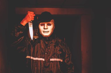 Cinayet, cinayet ve insan konsepti. Siyah giyen suçlu ya da katil. Cinayet mahallinde elinde bıçak tutan beyaz bir maske var.