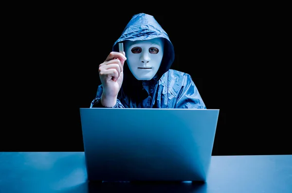 Anonymous computer hacker in white mask and hoodie. Obscured dark face holds a USB flash drive in his hands, Data thief, internet attack, darknet and cyber security concept, with copy space