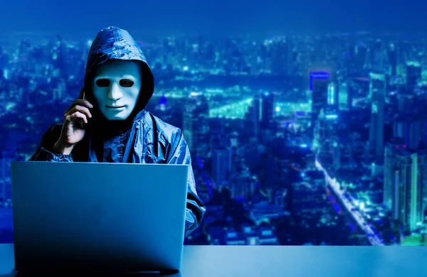 Beyaz maskeli ve kapüşonlu isimsiz bilgisayar korsanı. Siber saldırı için dizüstü bilgisayar kullanan ve modern şehir arka planında cep telefonu kullanan karanlık yüz, veri hırsızı, internet saldırısı, darknet ve siber güvenlik kavramı.