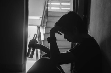 Eski dairede bir şişe alkollü bira tutan genç adamların silueti sağlıksız yaşam tarzı, bağımlı erkekler, yalnız oturan, şişeli bunalımlı adam, alkol bağımlısı....