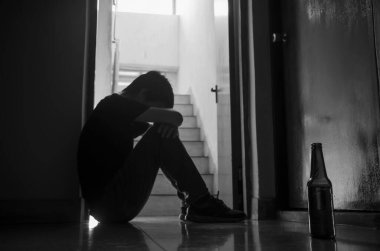 Bira ve alkol içen mutsuz bekâr genç adam kendini tükenmiş, yalnız ve çaresiz hissediyor acı ve duygusal stres, bağımlılık ve erkek depresyonu kavramı. Seçici odak noktası bira şişesi.