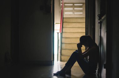 Yalnız oturan bir kız silueti, üzgün ve ciddi bir kadın dizine sarılıyor, yakın bir dairede, dramatik bir an. kopyalama alanı ile