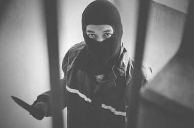 Ganimet için elinde bıçakla merdivenlerde yürüyen maskeli bir haydut.