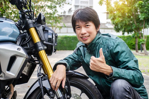 Dreams come true, Cheerful Handsome rider biker man in green leather jacket smiling to the camera joyfully showing thumbs up gesture in side a motorcycle outdoors