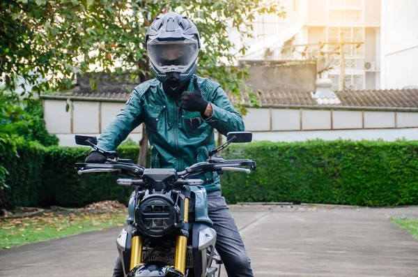 城市街道上穿着绿色皮夹克骑着摩托车大显身手的快乐的亚洲人的画像 — 图库照片