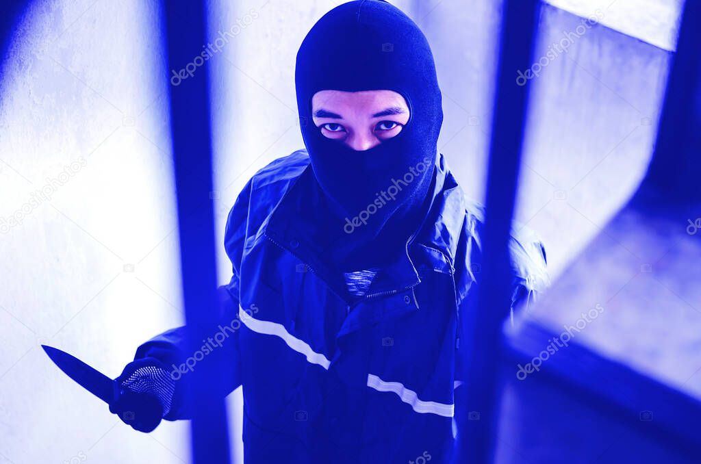 Bandit wearing a mask walking on stairs with a knife for the loot, focus is knife