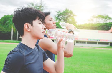 Koşudan sonra iki genç adam şişeden su içiyor. Dışarıda iki şişe soğuk içeceği olan genç adam.