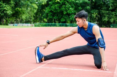Bir erkek sporcu ısınıyor, bir koşucu stadyumdaki yarış pistinde koşmadan önce bacaklarını esnetiyor.