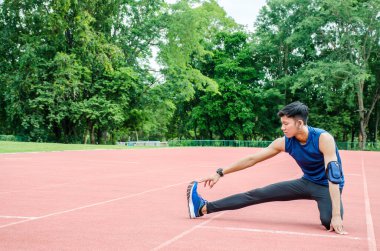 Bir erkek sporcu ısınıyor, bir koşucu stadyumdaki yarış pistinde koşmadan önce bacaklarını esnetiyor.