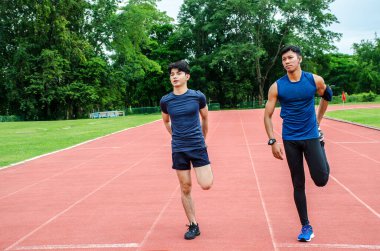 Antrenman takımı arkadaşları. İki erkek sporcu ısınıyor, iki koşucu stadyumdaki yarış pistinde koşmadan önce bacaklarını esnetiyor.