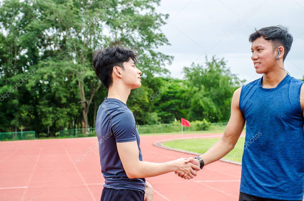 Two male athletes stand shake hands to cheer and create a good friendship. Before going out to run in the stadium. copy space.