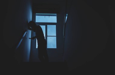 Karanlık evde, pencerenin önünde telefonu kullanan yalnız bir adam silueti. Adam tek başına pencerede duruyor. Depresyon ve endişe bozukluğu kavramı..