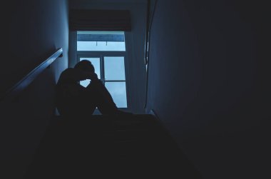 Siluet Üzgün genç adam karanlıkta merdivenlerde oturuyor, depresyon ve endişe bozukluğu konsepti, yaşam sorunları, hastalık, üzüntü, umutsuzluk, karanlık.