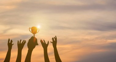 Birçok el kaldırıldı. Kazanan kupayı elinde tutuyor. Gün batımında birçok elin siluetleri.