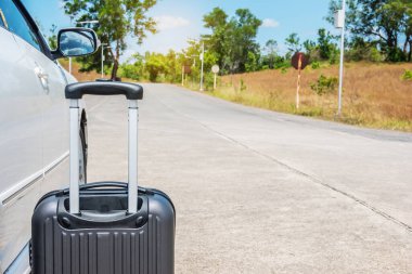 Siyah bavul yolda, beyaz bir arabanın yanında. Araba yolculuğuna hazırlık.