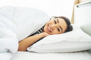 Genç ve güzel bir kadın sabahın erken saatlerinde beyaz yastığa uzanmış gülümsüyor.