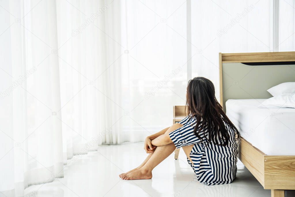 Sad asian woman lonely at home self isolation quarantine for COVID-19 Coronavirus social distancing prevention, She sitting on the floor near bed feeling boring in bedroom, Mental health.