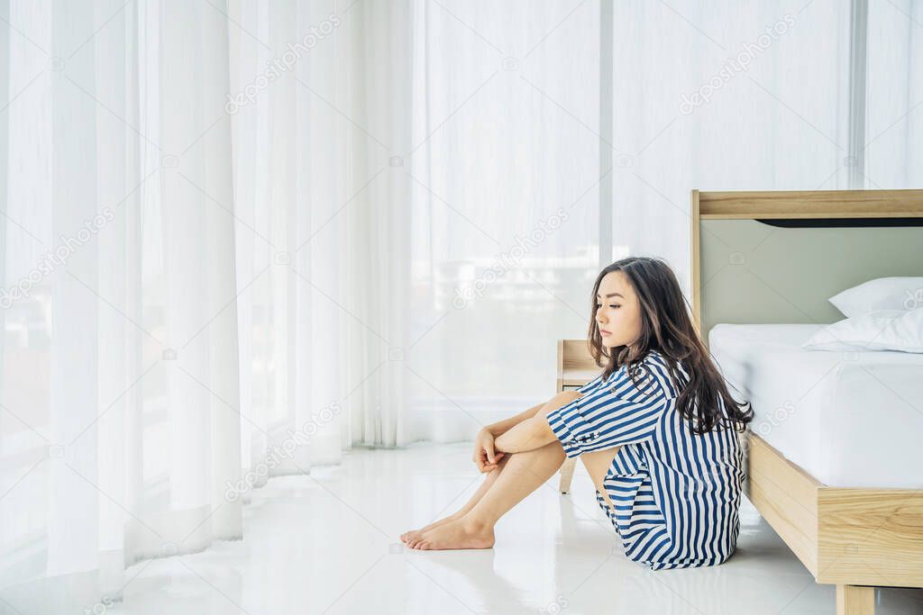 Beautiful asian woman sitting on the floor near bed feeling depressed stress in bedroom, Young woman suffers from insomnia