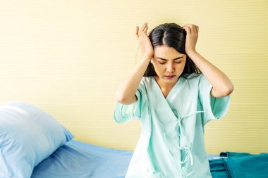 Asyalı genç kadın hastalar ellerinin alnında baş ağrısı çekiyorlar. Tıbbi ve sağlık hizmetleri konsepti. Hasta, kaşları çatık bir kadın hastane odasında yatakta oturuyor..
