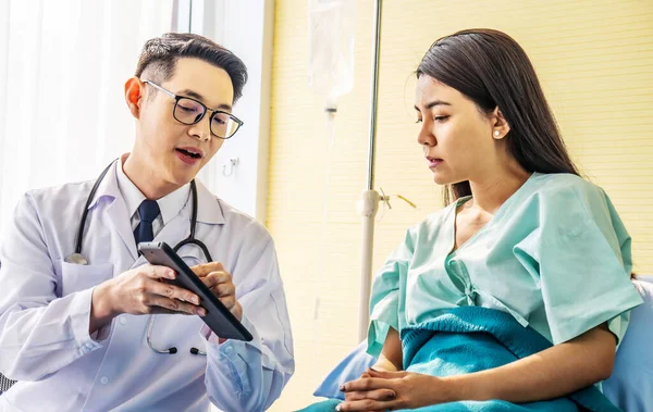 Asian male doctor talking to asian female patient in bed, while explaining exam results in computer to patient at medical consultation, Medicine and health care concept, selective focus point