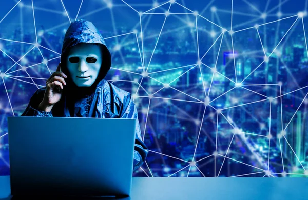 Beyaz maskeli ve kapüşonlu isimsiz bilgisayar korsanı. Siber saldırı için dizüstü bilgisayar kullanan ve modern şehir arka planında cep telefonu kullanan karanlık yüz, veri hırsızı, internet saldırısı, darknet ve siber güvenlik kavramı.