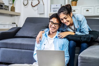 Gülümseyen genç bir çift evdeki kanepede oturup bilgisayardan keyif alırken mutlu bir adam ve kadın dizüstü bilgisayara bakıp gülüyor ya da internetten arıyor, komik videolar izliyorlar.