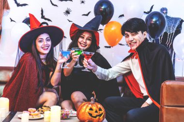 Asyalı Mutlu arkadaşlar Cadılar Bayramı kutlamalarında kostümlü ve makyajlı koltukta oturup kokteyl içerek ve partide eğlenerek Cadılar Bayramı 'nı kutluyorlar..