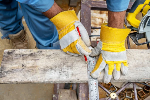 Construction worker wears protective leather gloves, with a pencil and the carpenter's square trace the cutting line on a wooden table. Construction industry, housework do it yourself.