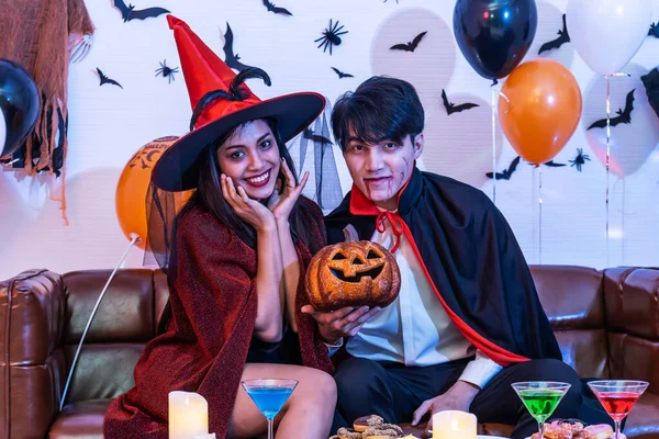 Asian Happy friends sitting on sofa in costumes and makeup on a celebration of Halloween smile in the room at home, Group of young people enjoying Halloween party with many items at home