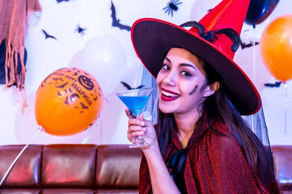 Beautiful asian young girl in witch costume having fun with cocktail drink alone at Halloween party by celebration, Pretty woman smiling and enjoying at home.