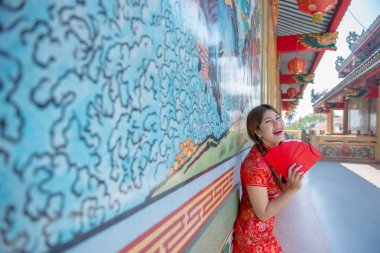 Cheongsam elbiseli güzel Asyalı kadının portresi elinde kırmızı bir zarf Taylandlı insanlar mutlu Çin yeni yılı konsepti