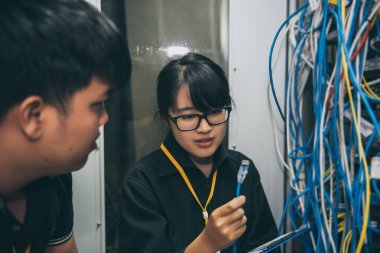 Sunucu odasında çalışan iki Asyalı mühendis bilgisayar ağlarının ve Tayland halkının bağlantılarını kontrol ediyor.