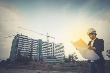 Genç Asyalı mühendis binanın kağıt planını arıyor.