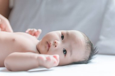 Sevimli Asyalı bebek yatağın ön tarafından uzanıyor.