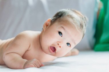 Sevimli Asyalı bebek yatağın ön tarafından uzanıyor.