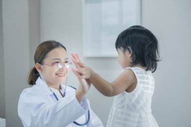 Solunumunu ve kalbini kontrol etmek için steteskop kullanan Asyalı bir doktor, Taylandlı çocukların sağlığını kontrol ediyor.