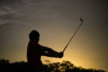 Siluet Asyalı golfçü Tayland halkının güzel günbatımında golf oynuyor.