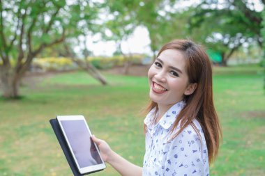 Güzel gülüşlü neşeli kadın parkta tablet oynuyor.