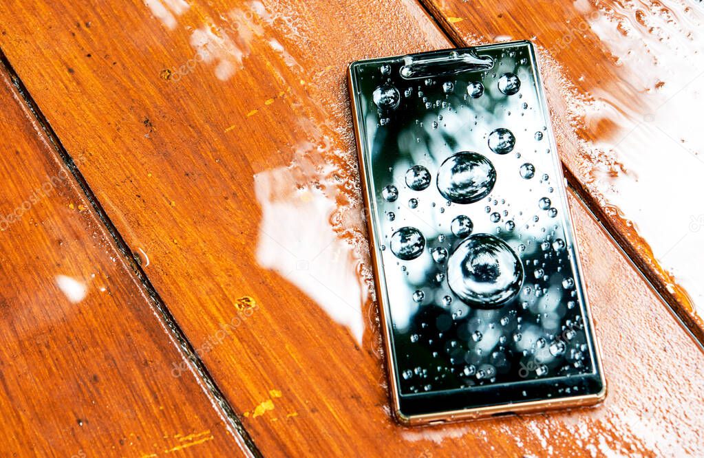 mobile phone with water drops on wet wooden background