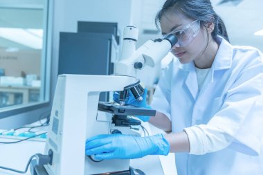 Genç Asyalı bilim adamı bir laboratuarda mikroskoptan bakıyor. Taylandlılar biraz araştırma yapıyor..