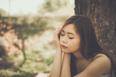 Asyalı üzgün kadını kapat. Ağaç bağcıklarının altında otur. Kalp kırıcı kız konsepti.