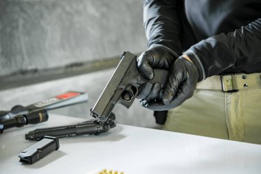 Elinde silahla siyah deri eldivenler giyen Asyalı bir erkek silaha kurşun dolduruyor.