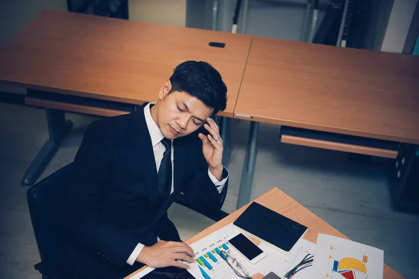 Asian businessman in black suit think idea for work at office,he work overtime alone in a company,dark tone,thailand people