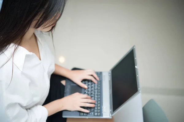 Asian woman working overtime late night in the office, light from the lamp for work, working with laptop on the leg and sitting the desk