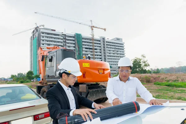 两名亚洲工程师正在看大楼的平面图 在车篷上 讨论了施工中的问题及解决办法 — 图库照片