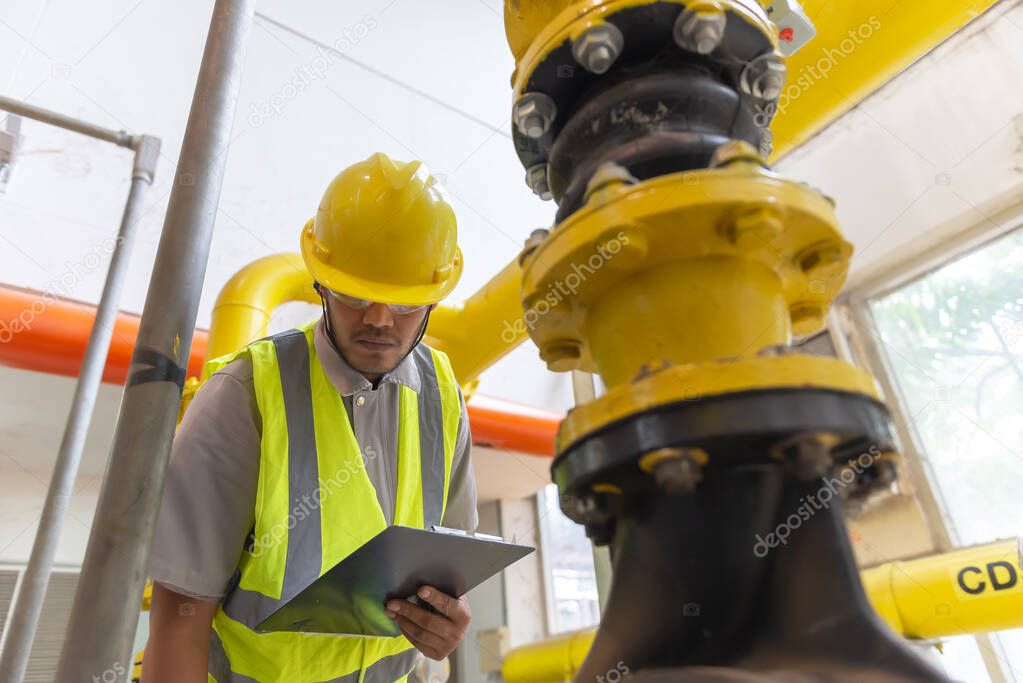 Asian engineer wearing glasses working in the boiler room,maintenance checking technical data of heating system equipment,Thailand people