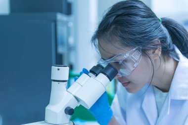 Genç Asyalı bilim adamı bir laboratuarda mikroskoptan bakıyor. Taylandlılar biraz araştırma yapıyor..