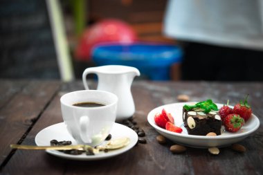 Beyaz tabakta taze çilekli Brownie, ahşap fonda sıcak kahve.