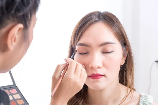 Makeup artist is makeup a asian woman model on white background,Before take a photo in studio