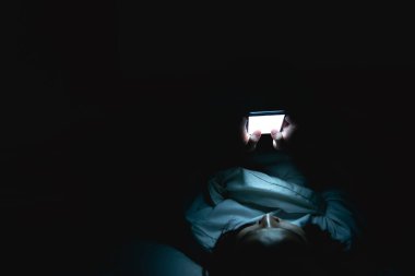 Asyalı kadın gece yatakta akıllı telefonla oyun oynuyor, Taylandlılar, sosyal medya bağımlısı.